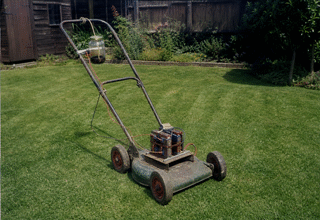An old petrol rotary lawnmower converted with a homemade magnet-motor where the engine was, a small box of coils bolted on top, on a very neatly mown lawn.